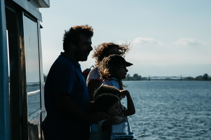 Silhouettes of a family standing on a boat, overlooking a calm body of water.