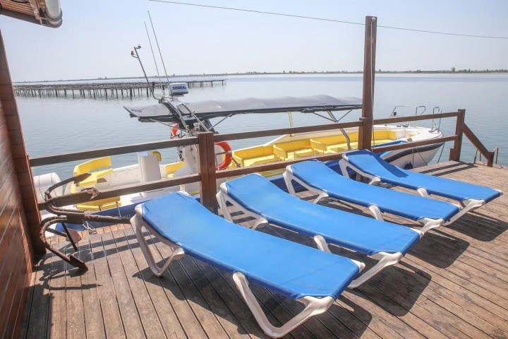 Four blue loungers on a wooden deck overlooking a boat and calm water.