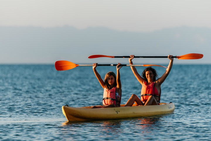 Two women in life jackets raising paddles while kayaking on a calm sea.