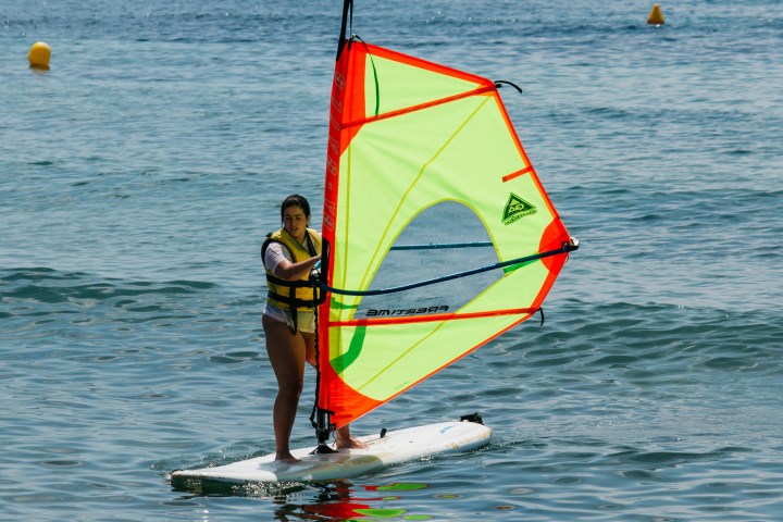 Person windsurfing on calm sea with a bright green and orange sail.