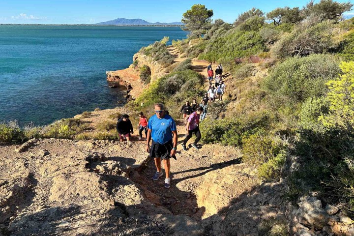 Group of people hiking along a coastal rocky path with a view of the ocean.